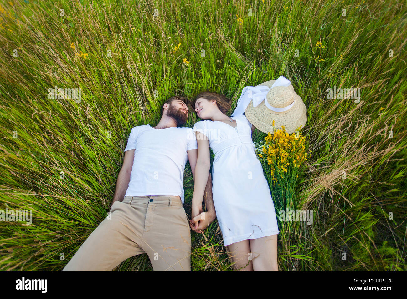 Happy young relaxed couple in love laying down on the grass overhead Stock Photo