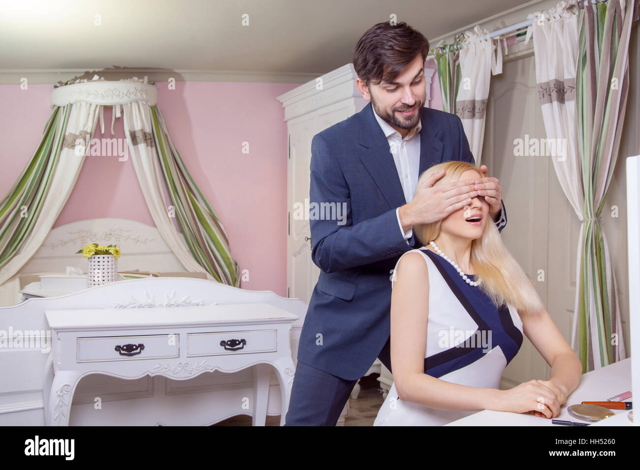 Young handsome man covering the eyes of beautiful surprised girlfriend and make her to guess who is there. Stock Photo