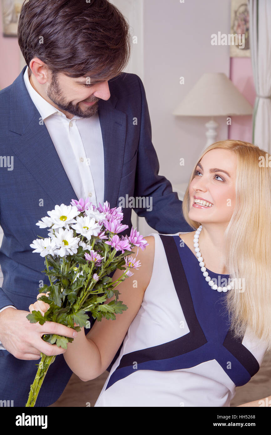 Young handsome man surprising her beautiful girlfriend and gives her bouquet of purple white flowers. Stock Photo