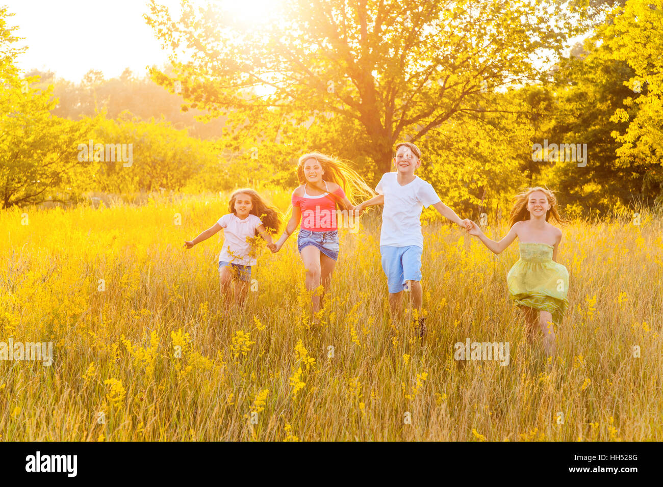 four happy beautiful children running playing moving together in the beautiful summer day. jumping and looking at camera. Stock Photo