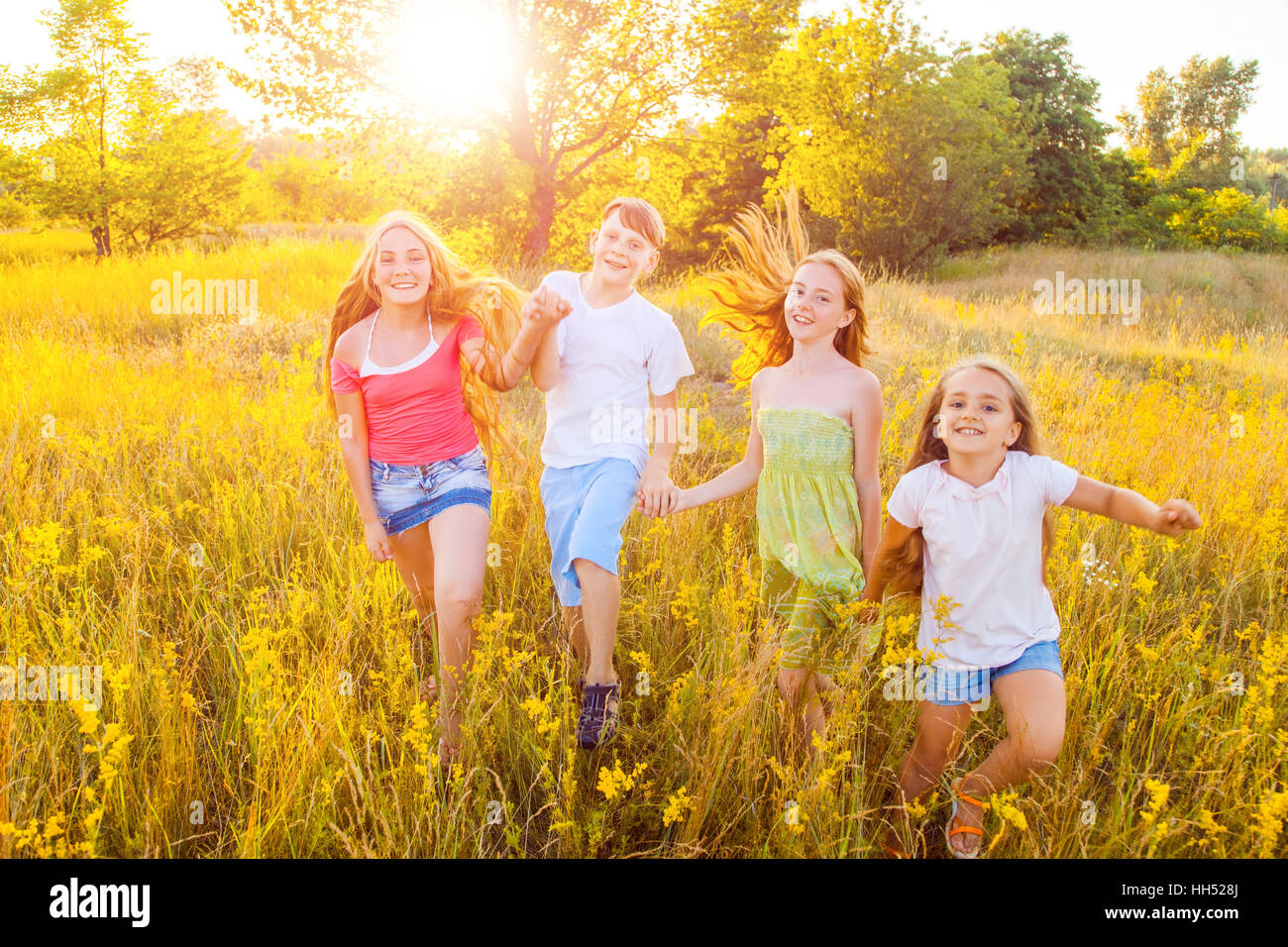 four happy beautiful children running playing moving together in the beautiful summer day. jumping and looking at camera. Stock Photo