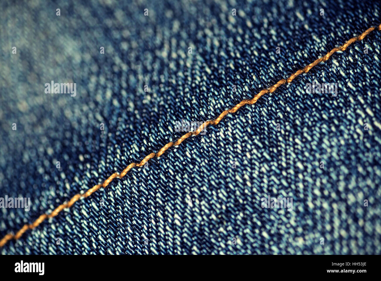 Macro closeup of yellow stitch on a pair of faded denim jeans. The thread on the material runs in a diagonal slant. Stock Photo
