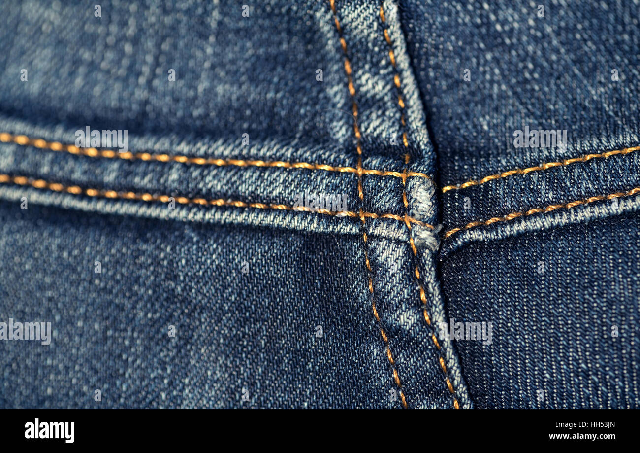 Macro closeup of yellow stitch on a pair of faded denim jeans in a cross position. The jaded jean material is aged and worn. Stock Photo