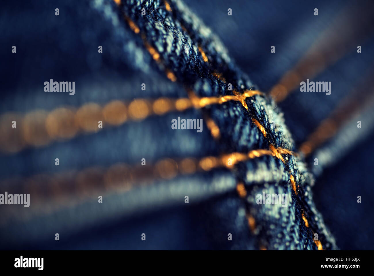 Macro closeup of yellow stitch on a pair of faded denim jeans creating an abstract zoom on the faded material. Stock Photo