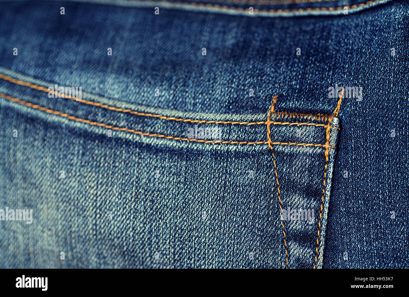 Macro closeup of yellow stitch on a pair of faded denim jeans. Stiching is of the back pocket corner. Stock Photo