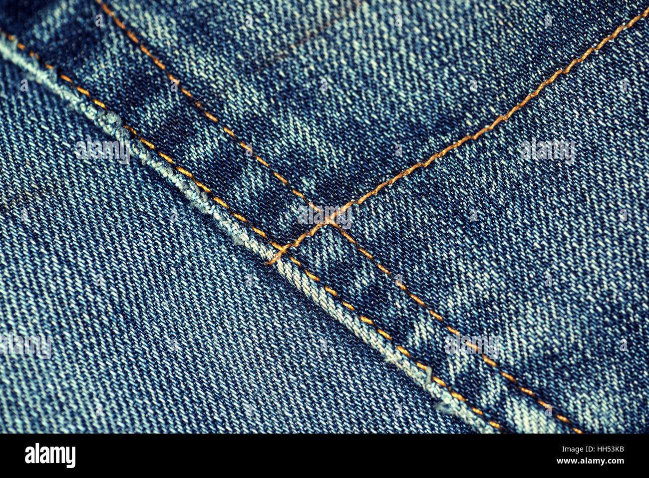 Macro closeup of yellow stitch on a pair of faded denim jeans with worn pocket edges. Stock Photo