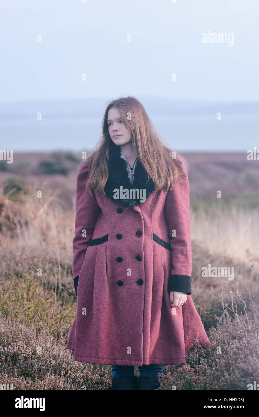 a young woman in a read coat is standing in the heather in winter Stock Photo