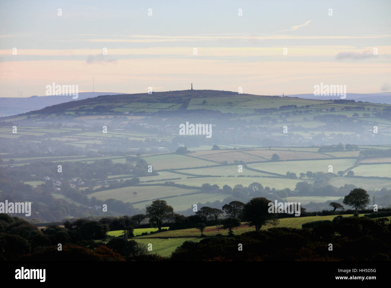 A view of fields and a distant hill shrouded in mist. Stock Photo
