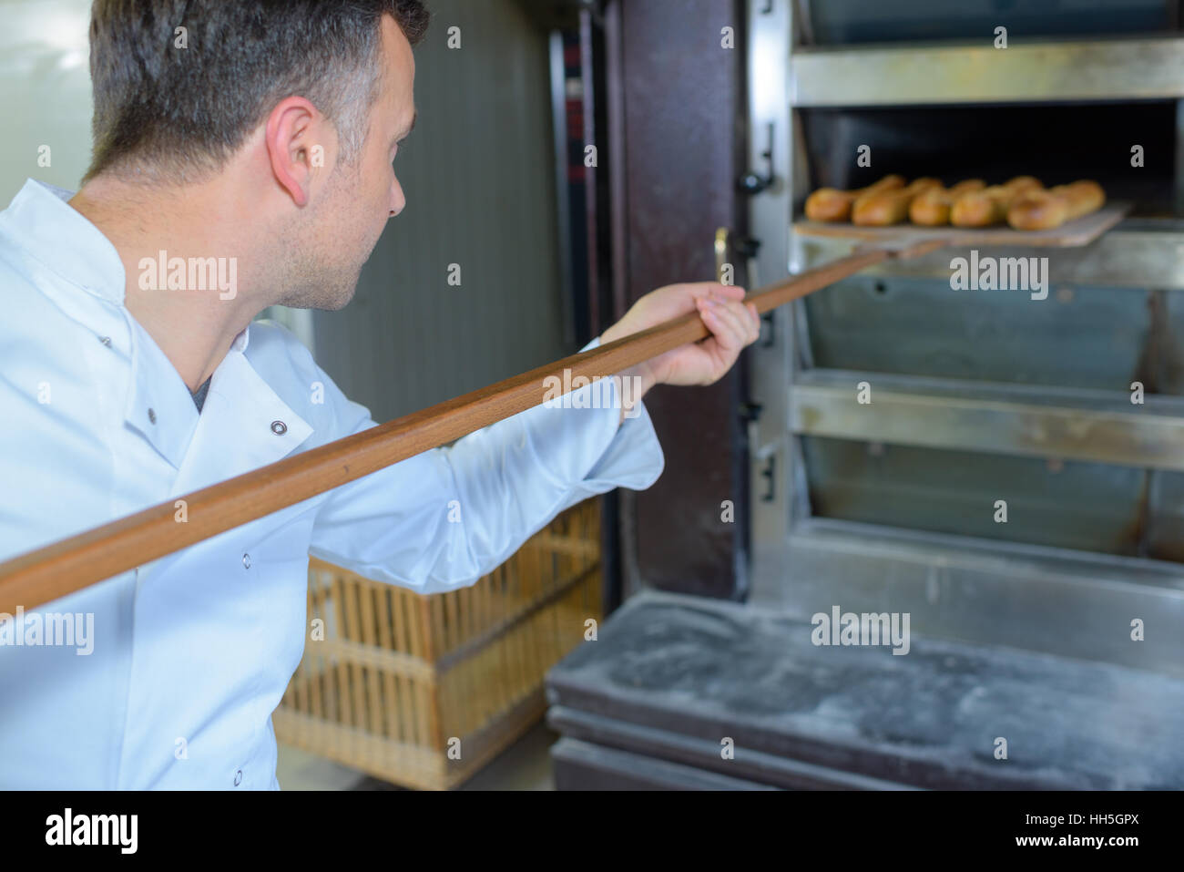Baker removing bread from oven Stock Photo - Alamy