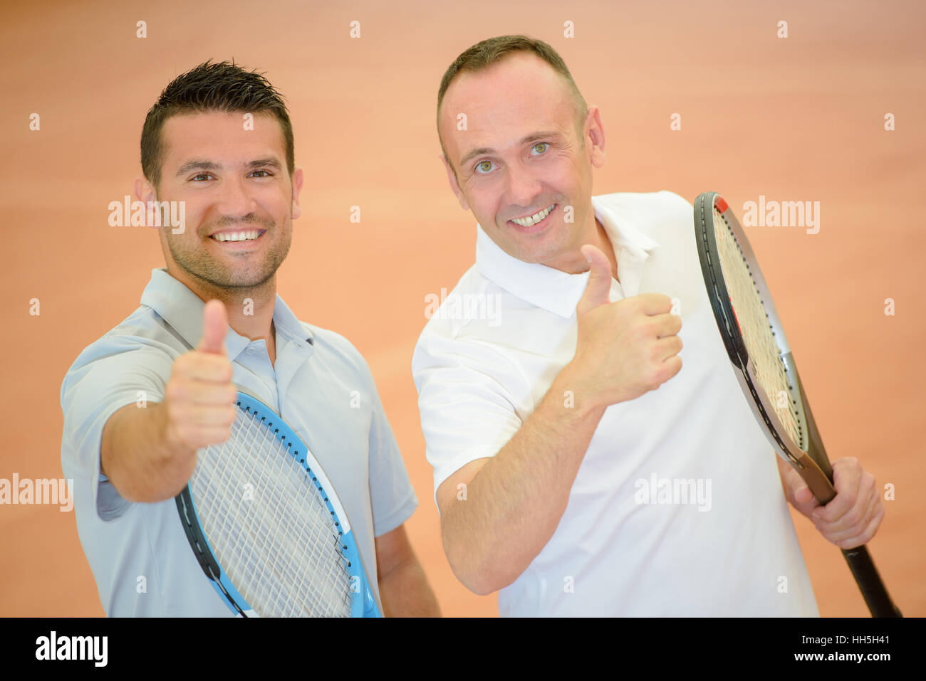 Two men holding tennis rackets making thumbs up gesture Stock Photo - Alamy