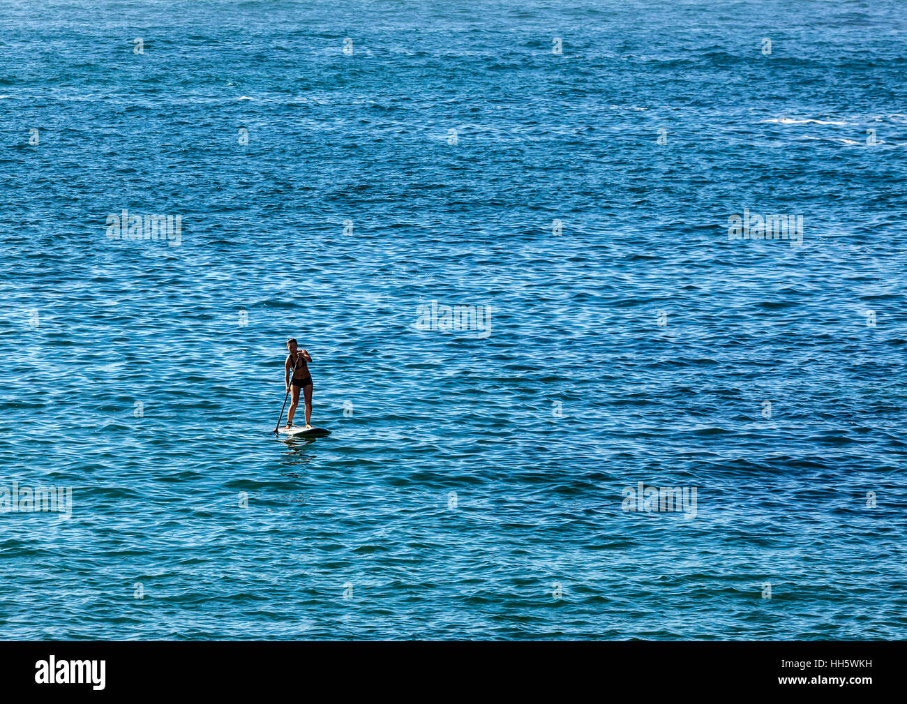 Lone young woman paddle boarding on smooth sea far from shore Stock Photo