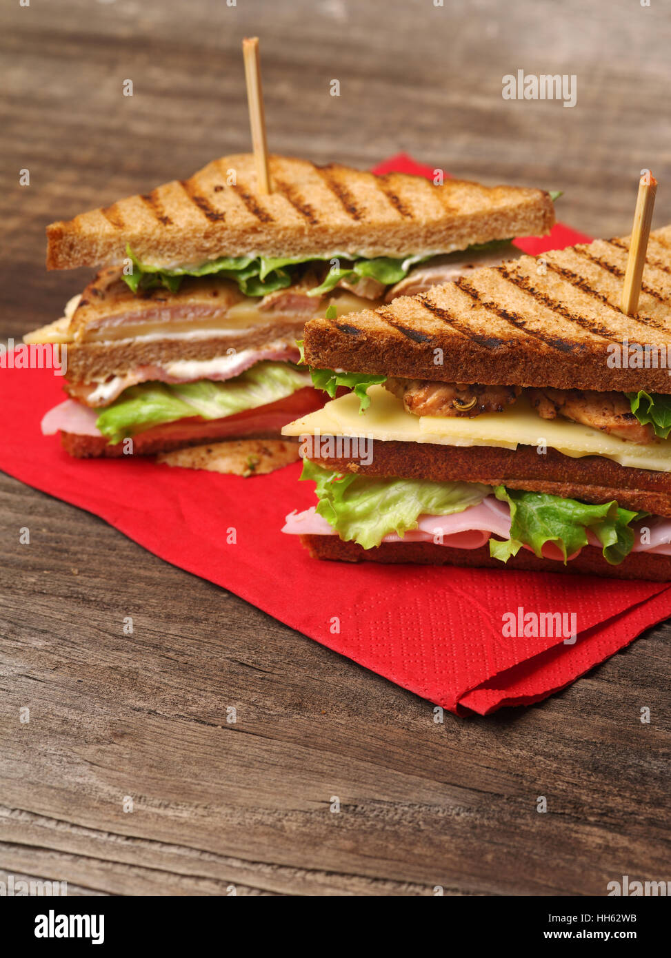 Photo of a club sandwich made with turkey, bacon, ham, tomato, cheese, lettuce on a red napkin and old wood picnic table. Stock Photo