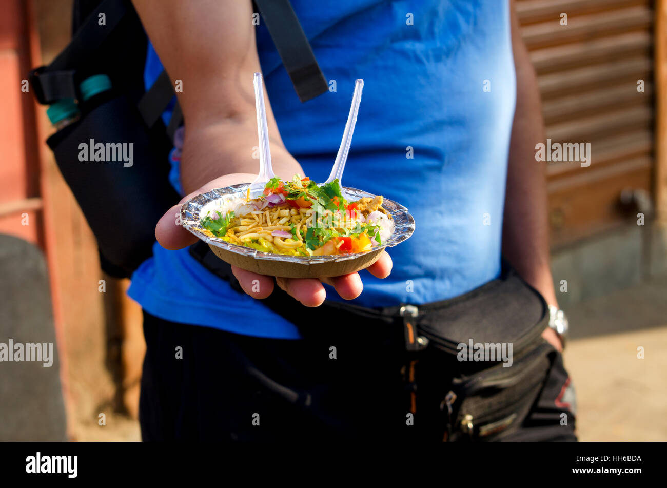 The man holds in hand a plate with street Indian food, the man,holds,a plate,street,the food,on a hand,offers,shows,national Stock Photo