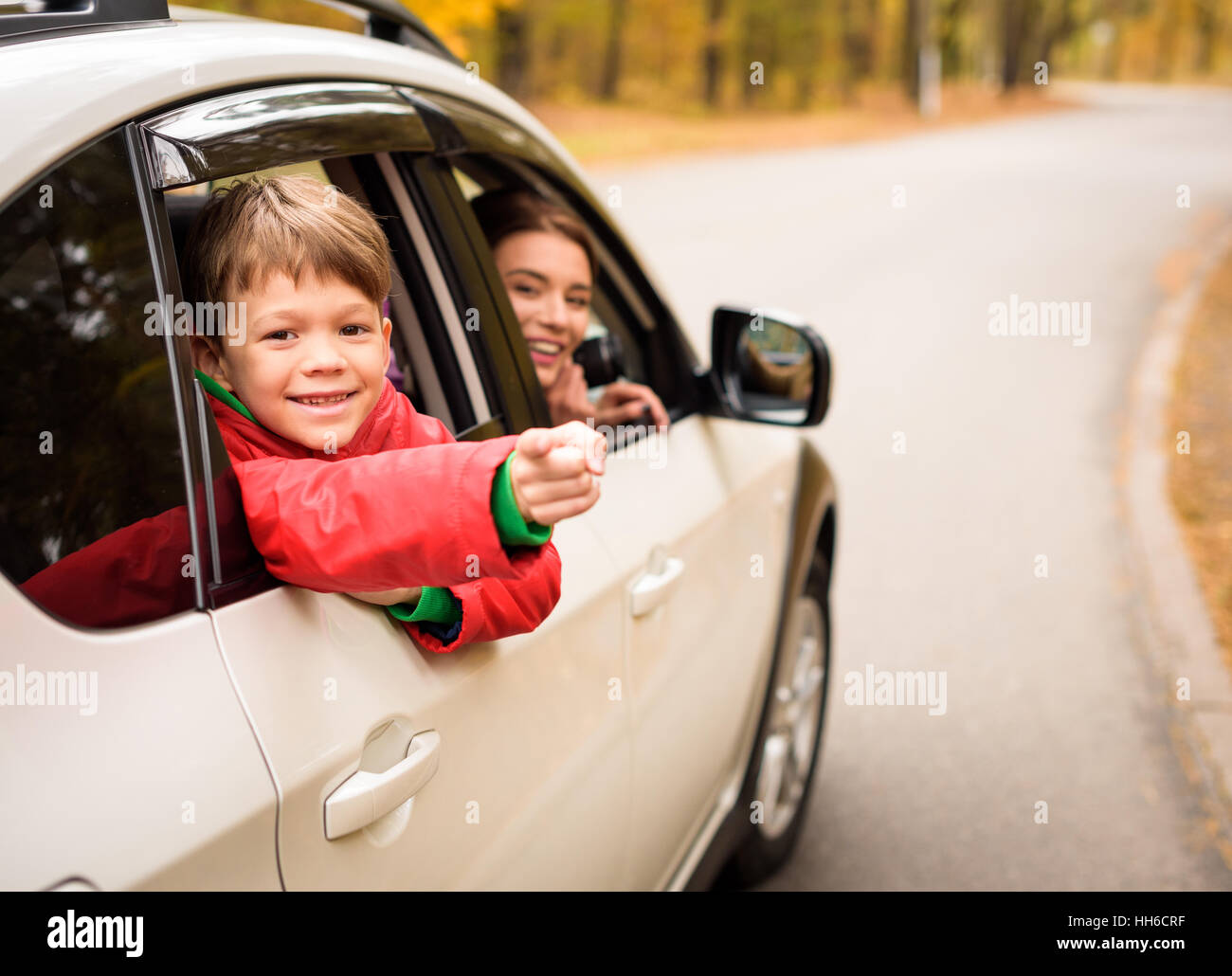Cute smiling boy looking through car window while traveling with parents in autumn forest Stock Photo