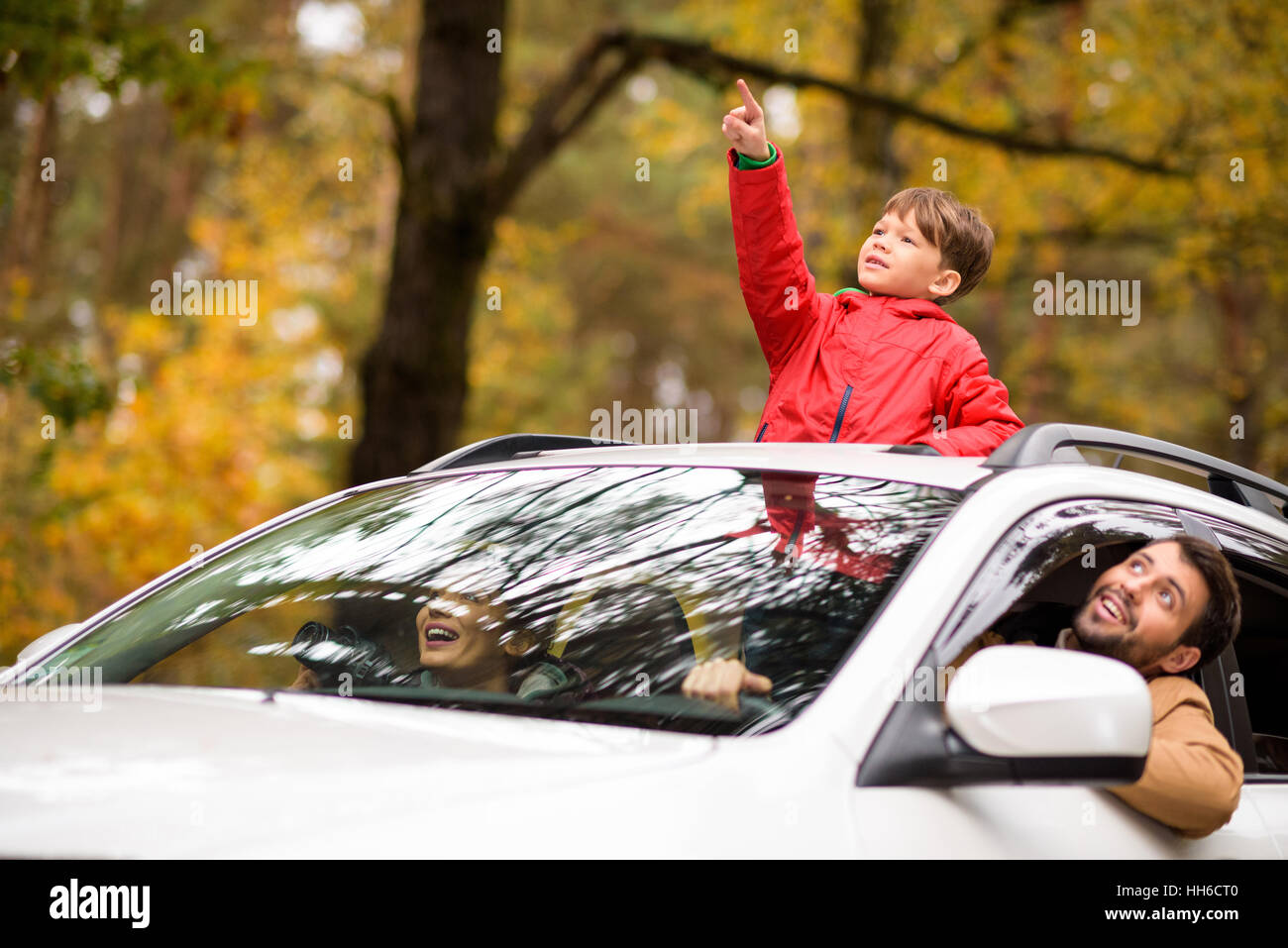 Adorable smiling boy standing in open car sunroof during family trip in autumn forest Stock Photo