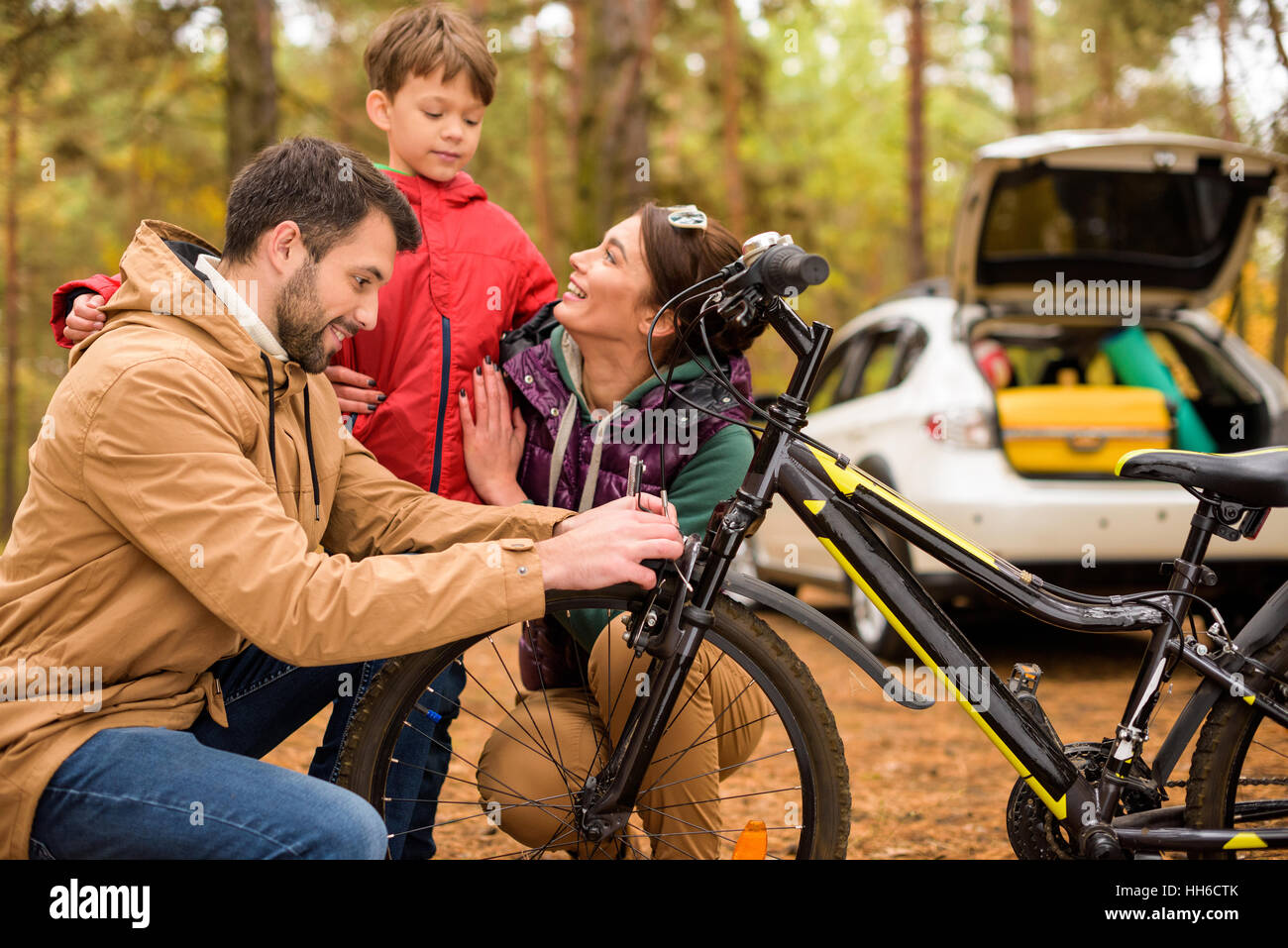 Happy family with bicycle in autumn forest with white car on background Stock Photo