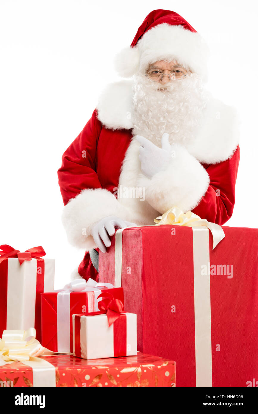 Happy Santa Claus standing with a pile of Christmas gifts isolated on white Stock Photo