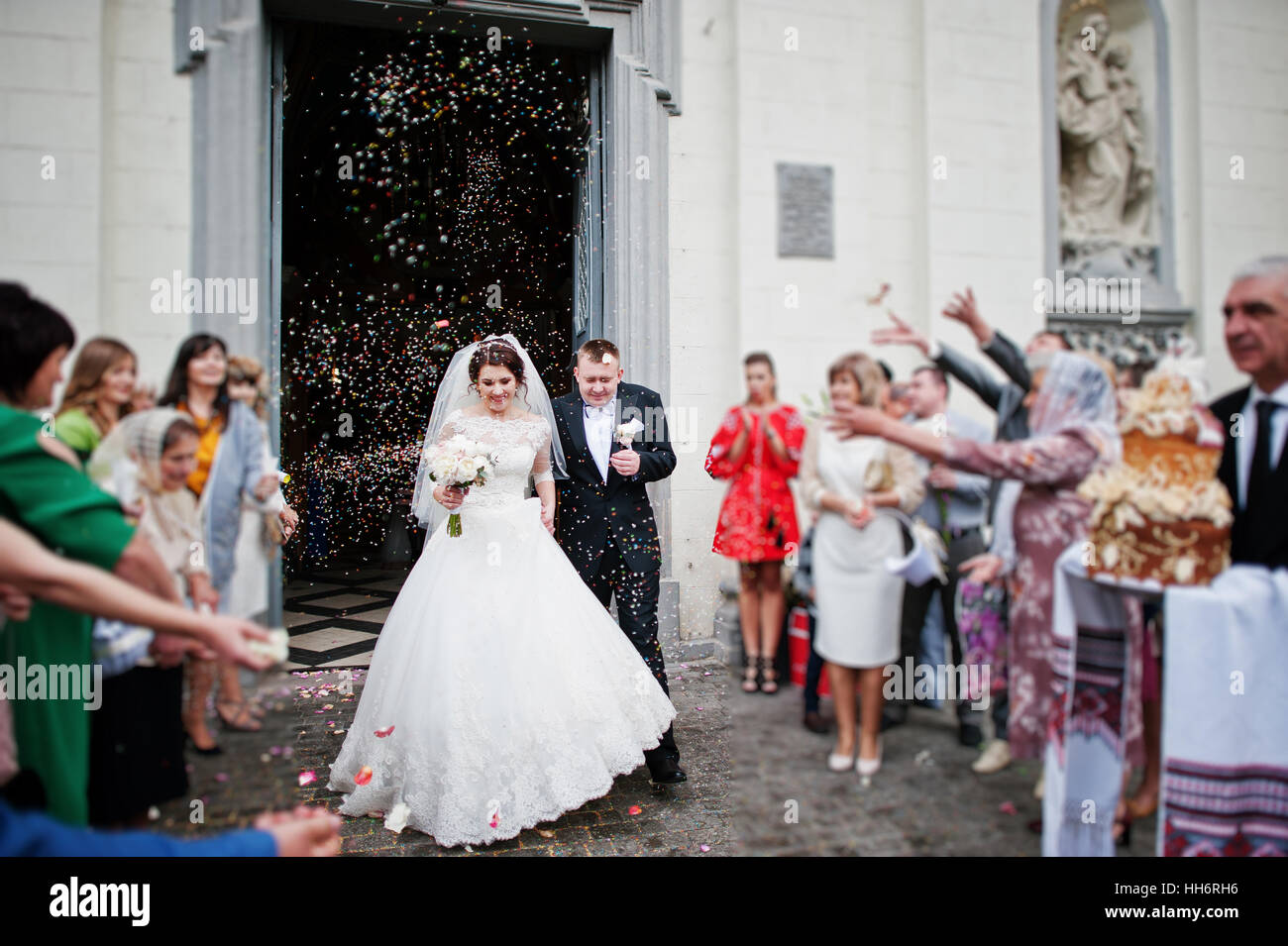 Happy wedding couple walking under colored rice which is thrown away ...
