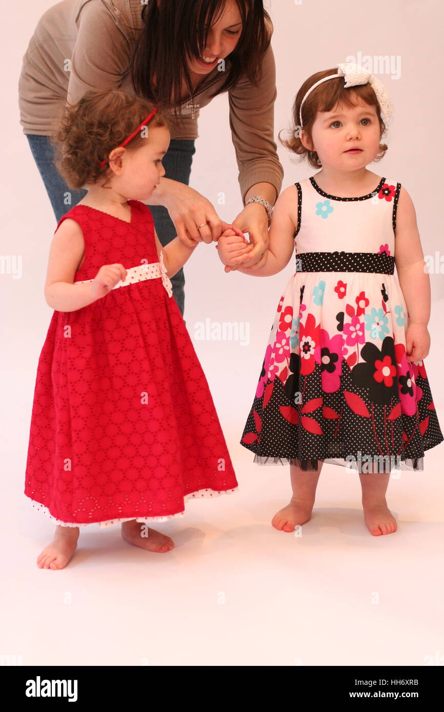 Two Little baby girls wearing dresses and hairbands looking at each ...