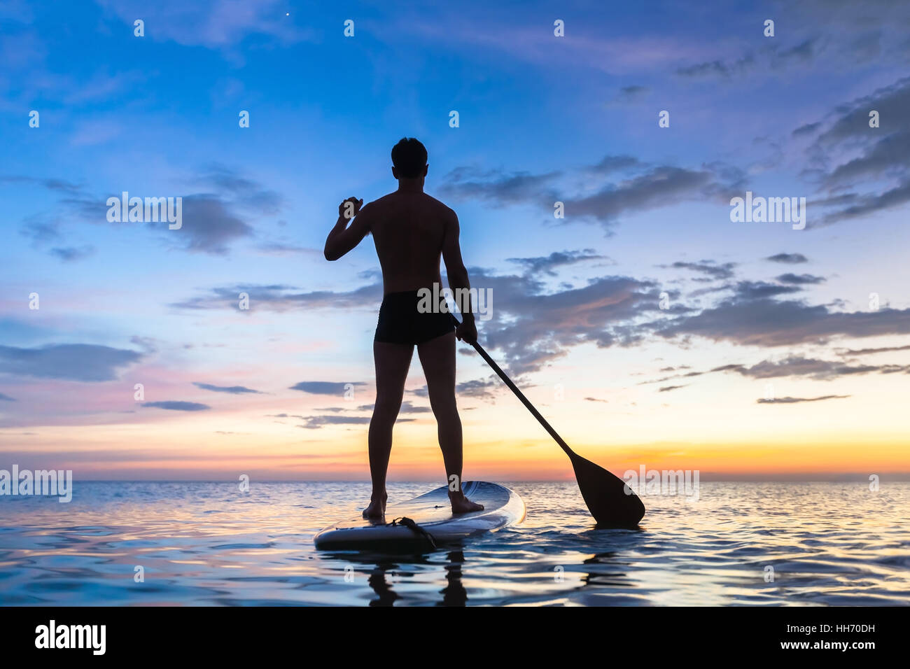 Silhouette of stand up paddle boarder paddling at sunset on a flat warm quiet sea Stock Photo