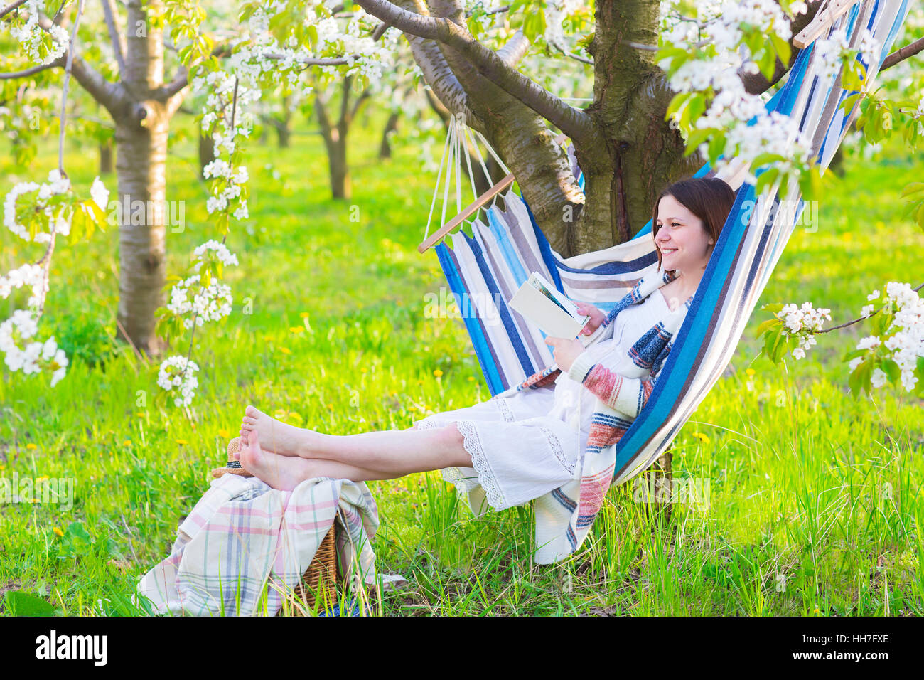 Beautiful pregnant woman sitting in hammock in blooming garden. Lazy