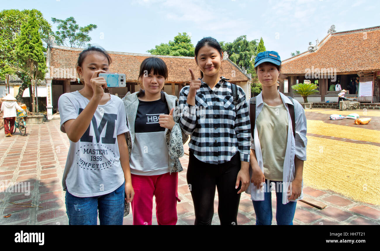 Teenage school girls visiting  Mong Phu communal house, Duong Lam Village. Corn crop drying.   Working on School project. Stock Photo