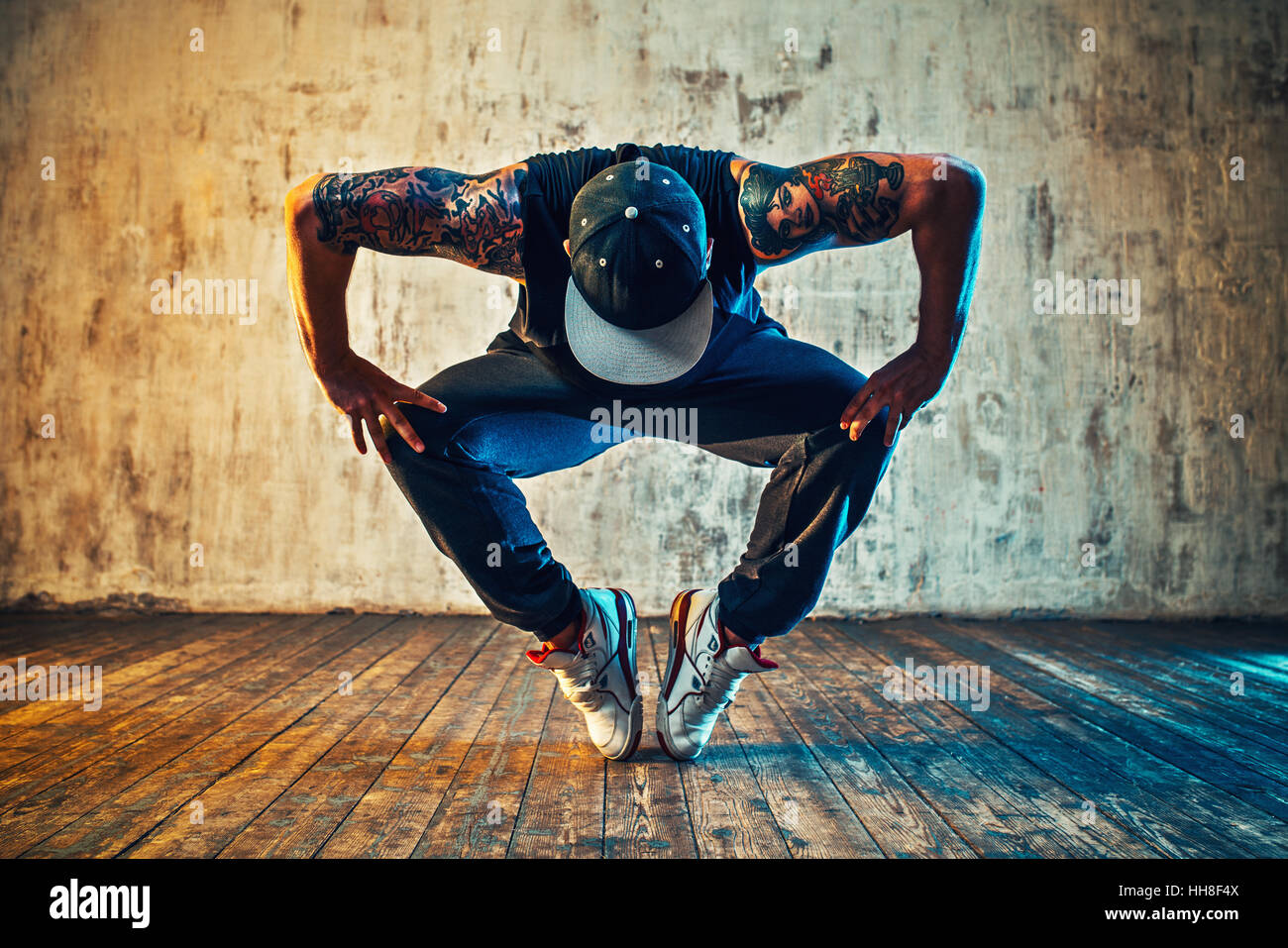 Young man break dancing on wall background. Blue and yellow colors tint. Tattoo on body. Stock Photo