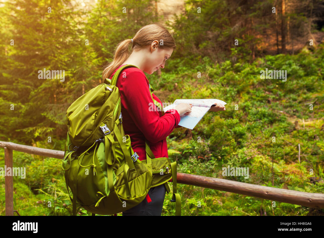 Young woman tourist with map and backpack navigating in forest at summer season Stock Photo