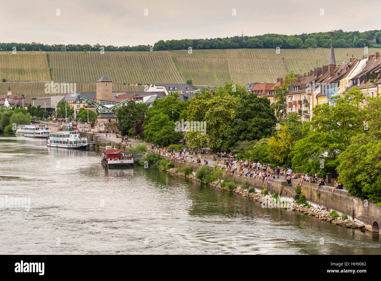 People sitting at the bank of the Main River in the evening in Wurzburg, Lower Franconia, Bavaria, Germany Stock Photo