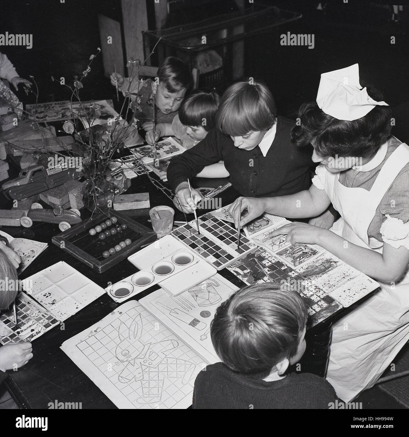 1950s, historical, a uniformed female nurse in a children's hospital  sitting, helping the small children with their water colour painting. Stock Photo