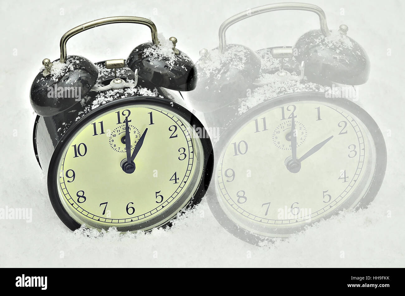 close up of two black retro alarm clocks, showing winter time, 1 am and 2 am on snow background Stock Photo