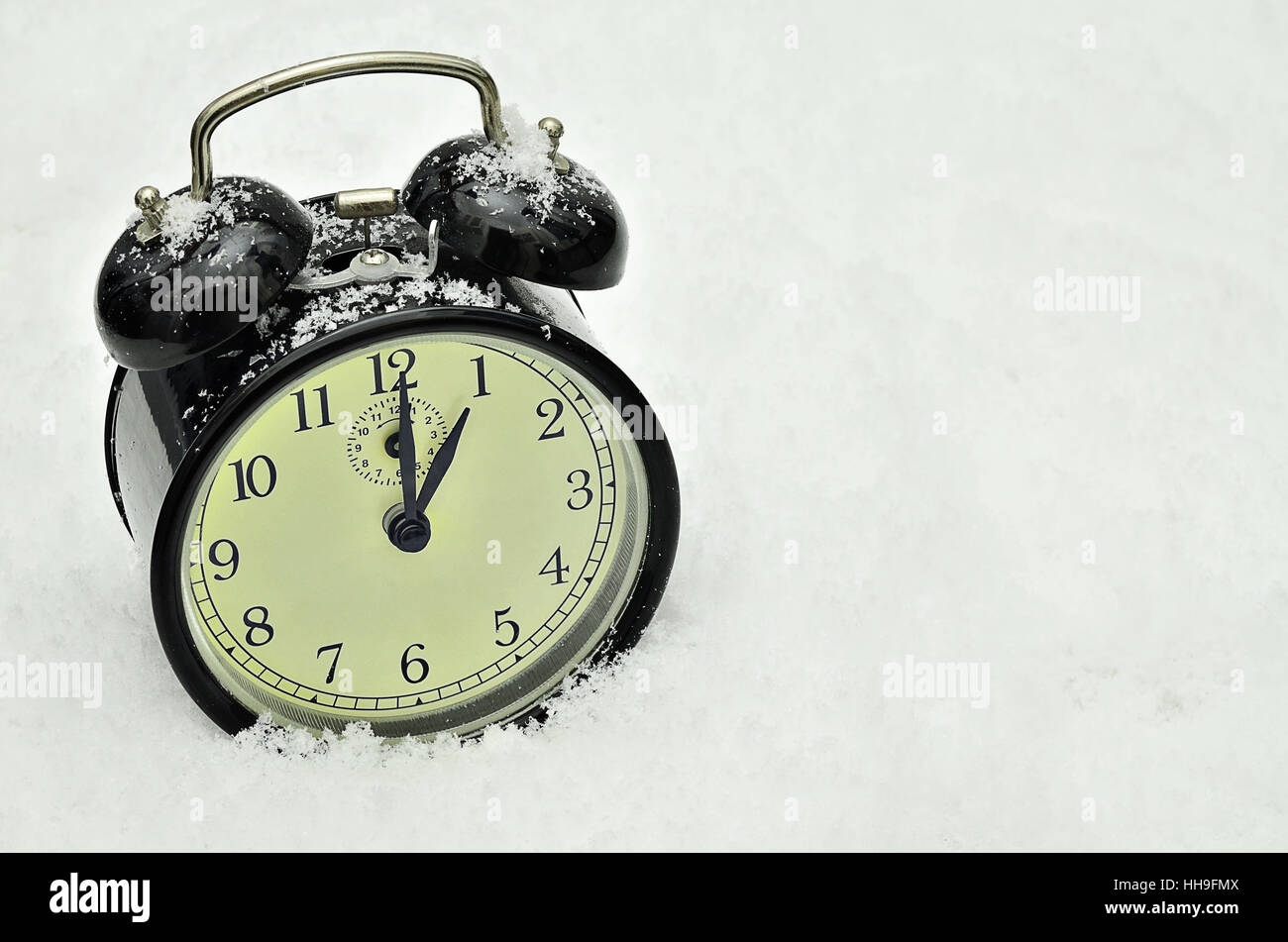 close up of a black retro alarm clock, showing winter time, 1 am, on snow background Stock Photo