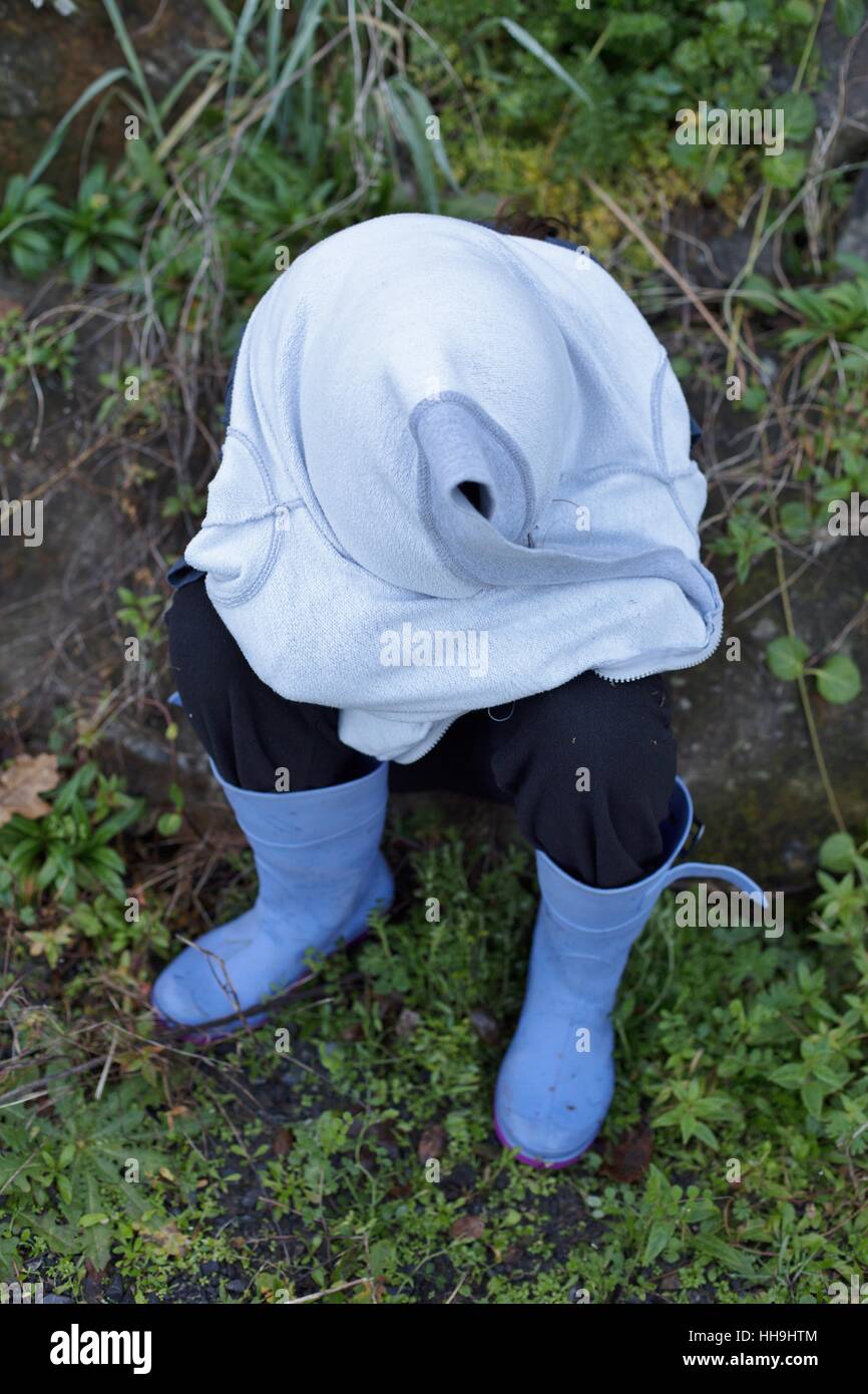 A young girl sitting outdoors, hiding herself in her own sweatshirt. Stock Photo