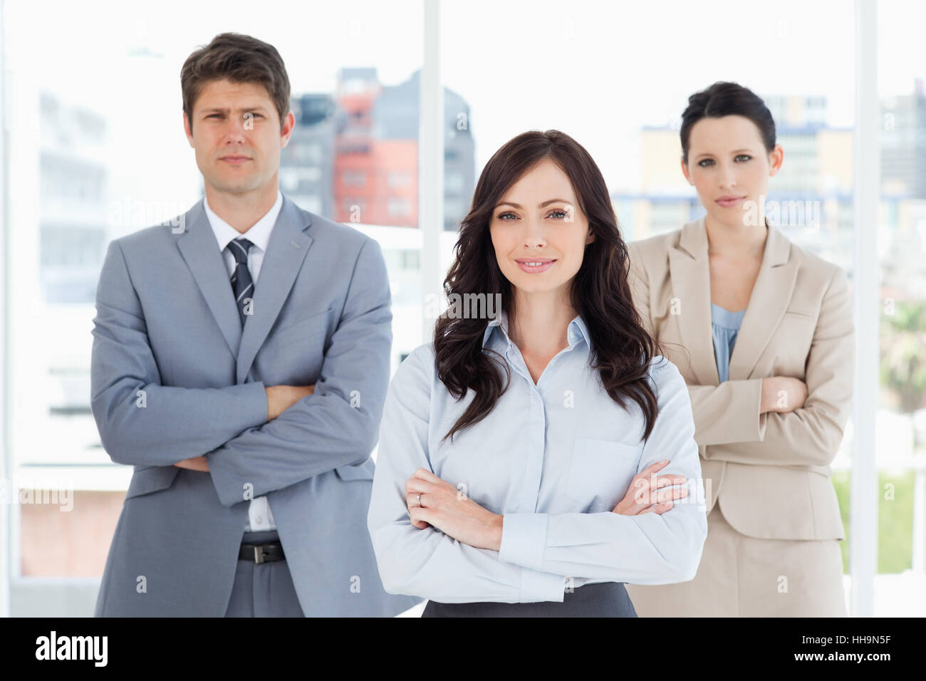 Three smiling business people crossing their arms in front of a window ...