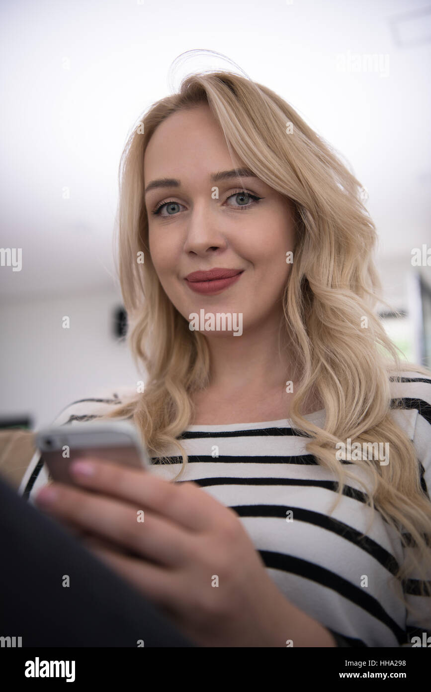 young happy woman sitting on sofa with mobile phone at luxury home ...