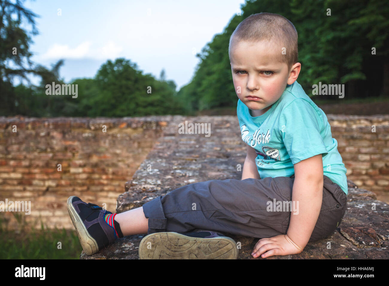Sad and angry boy sitting on a brick wall Stock Photo
