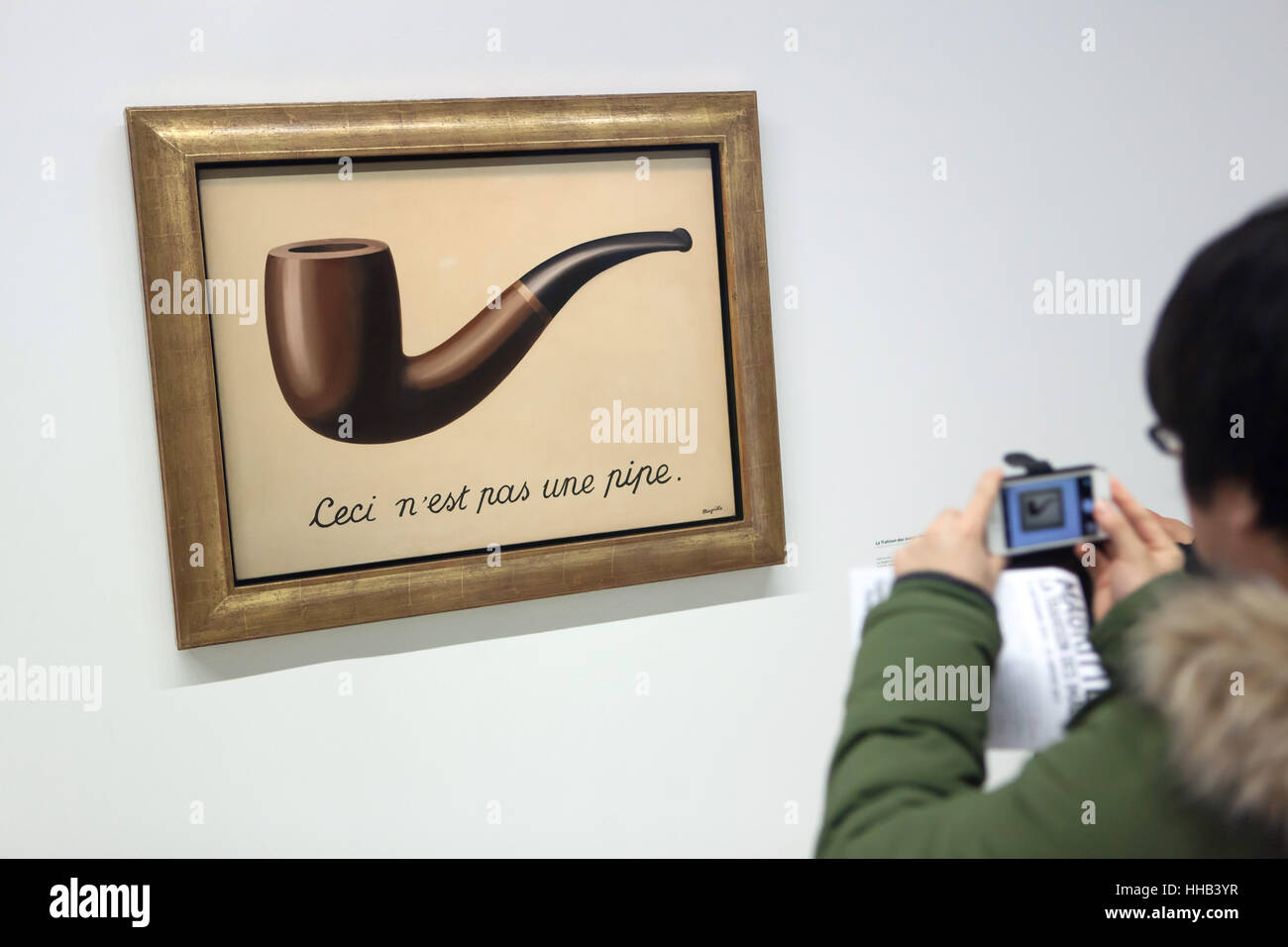 Visitor uses his smartphone to photograph the painting 'La trahison des images' ('The Treachery of Images') by Belgian surrealist artist Rene Magritte (1929) displayed at his retrospective exhibition in the Centre Pompidou in Paris, France. The French inscription 'Ceci n'est pas une pipe' means 'This is not a pipe'. The exhibition entitled 'Rene Magritte. The Treachery of Images' runs till 23 January 2017. After that the reformulated version of the exhibition will be presented at the Schirn Kunsthalle in Frankfurt am Main, Germany, from 10 February to 5 June 2017. Stock Photo