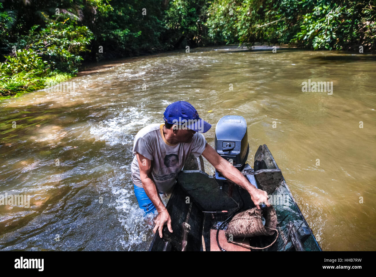 A boat motorist pushing the boat to move on shallow water in the river, through a customary forest in Kapuas Hulu, West Kalimantan, Indonesia. Stock Photo