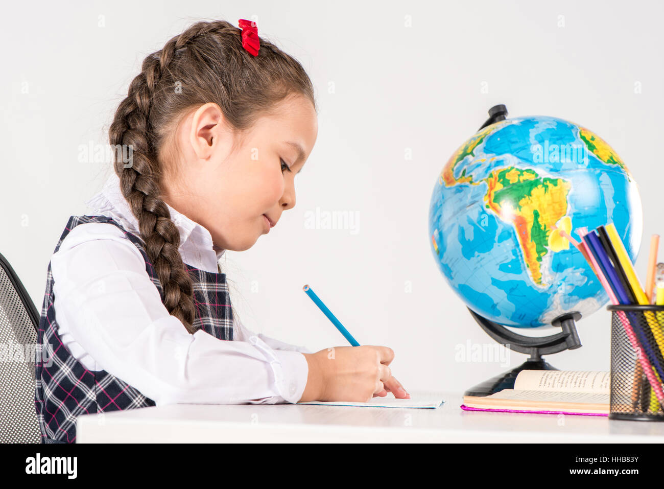 Schoolgirl writing homework with globe behind her on grey Stock Photo