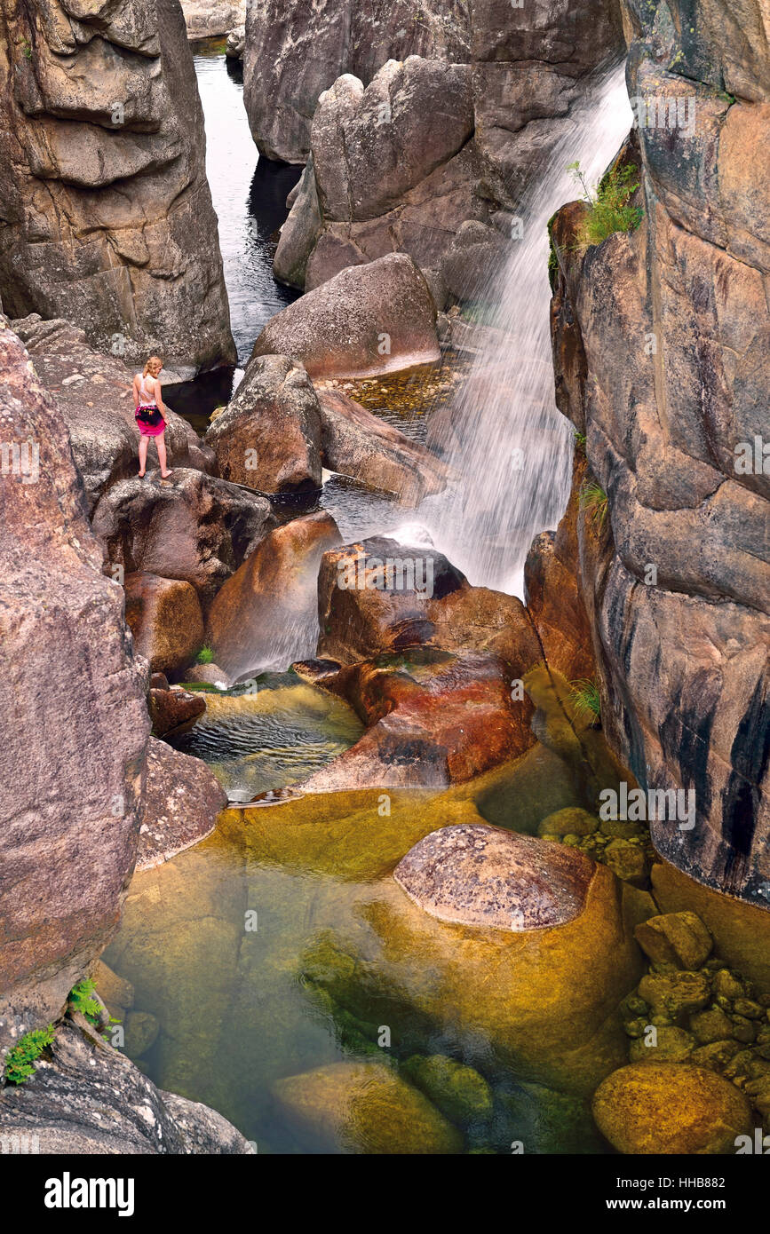 Girl standing on a rock next to waterfall in wild mountain ravine Stock Photo