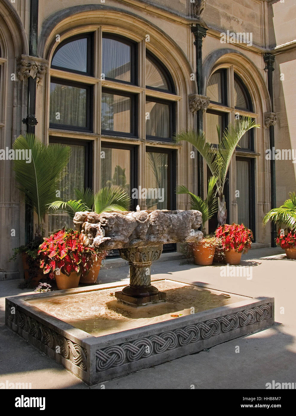 Outdoor patio on the Biltmore estate showiing large windows and outdoor foliage ornate fountain  and red flowers bordering patio Stock Photo