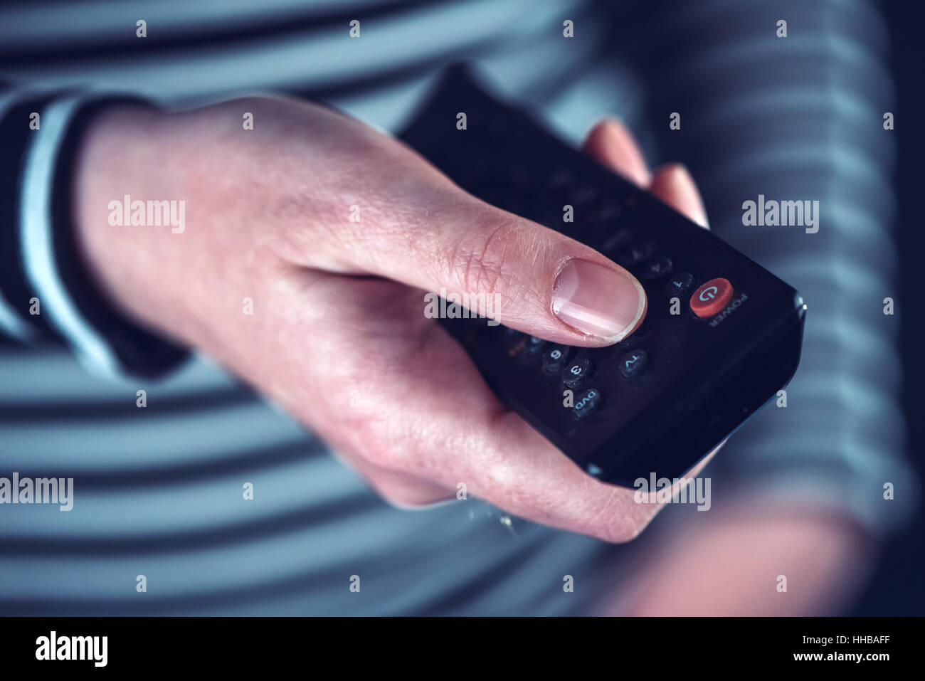 Female hand with television remote control pointing to tv set and turning it on or off Stock Photo