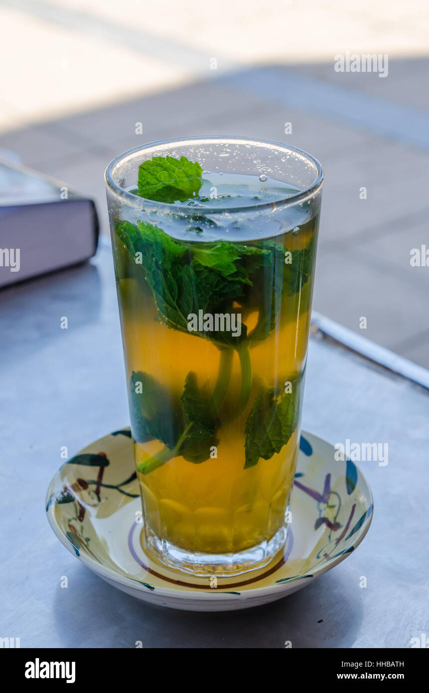Traditional sweet Moroccan tea with mint leaves in tall glass on outside table, Morocco, North