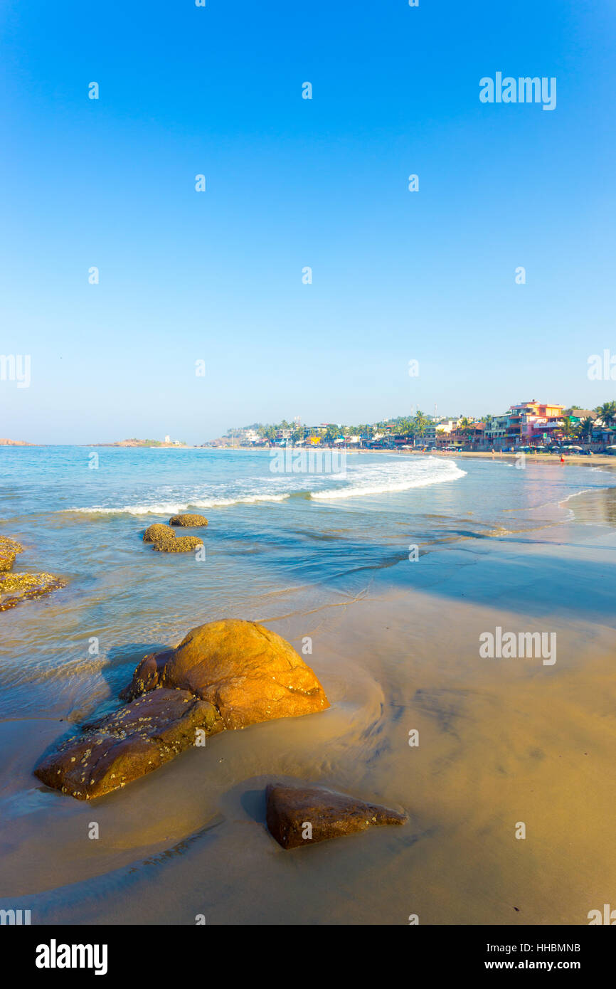 Hotels line the beachfront above the sand at Light House Beach and ocean waves at a tourist town in Kerala, India. Vertical Stock Photo