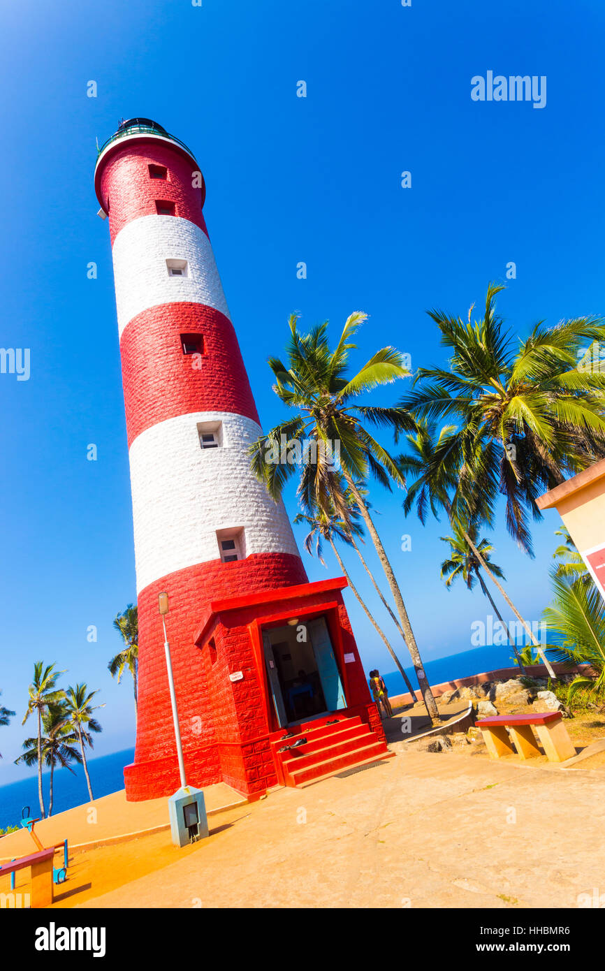 Closeup of red and white striped lighthouse surrounded by palm trees at Kovalem Beach in Kerala Stock Photo