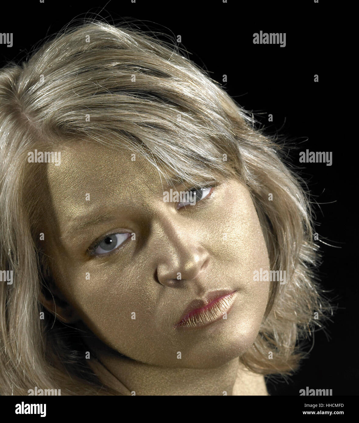 sad lookong girl with golden bodypainted face in black back Stock Photo