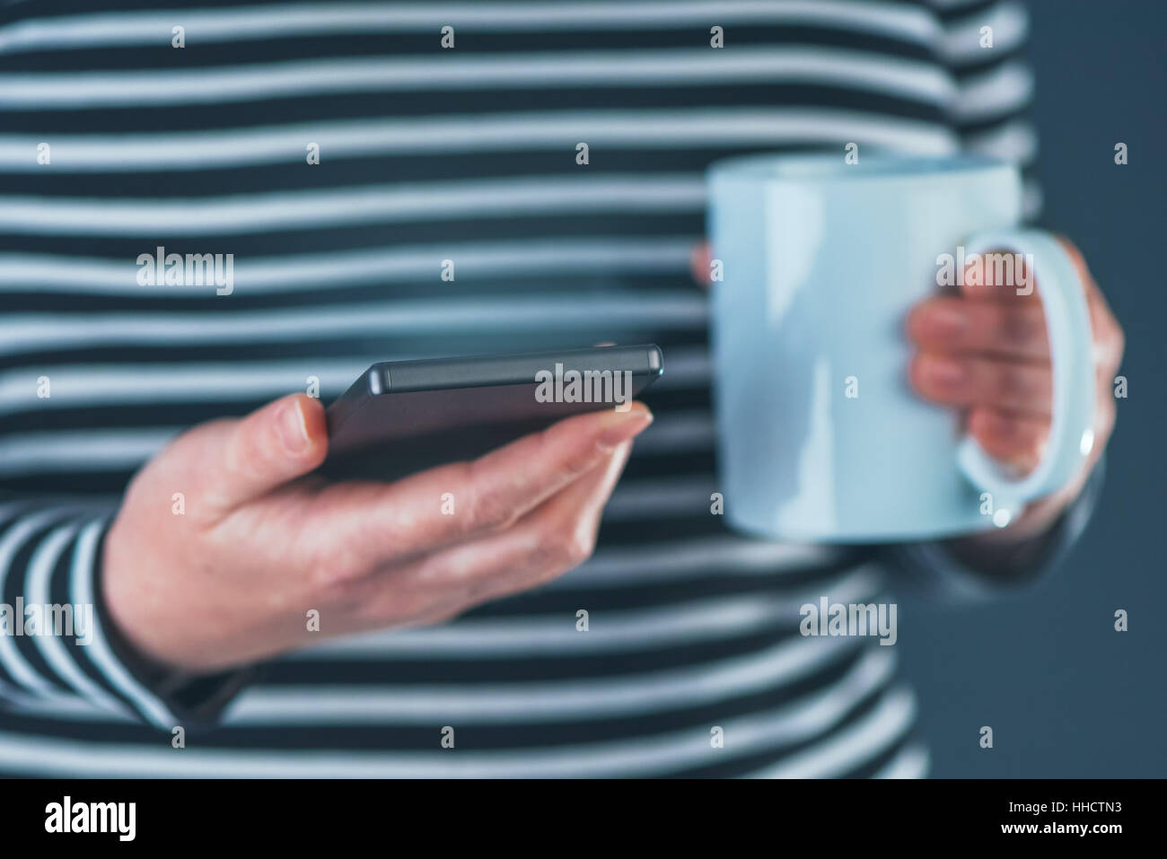 Woman drinking coffee and reading SMS on mobile phone, close up with selective focus Stock Photo