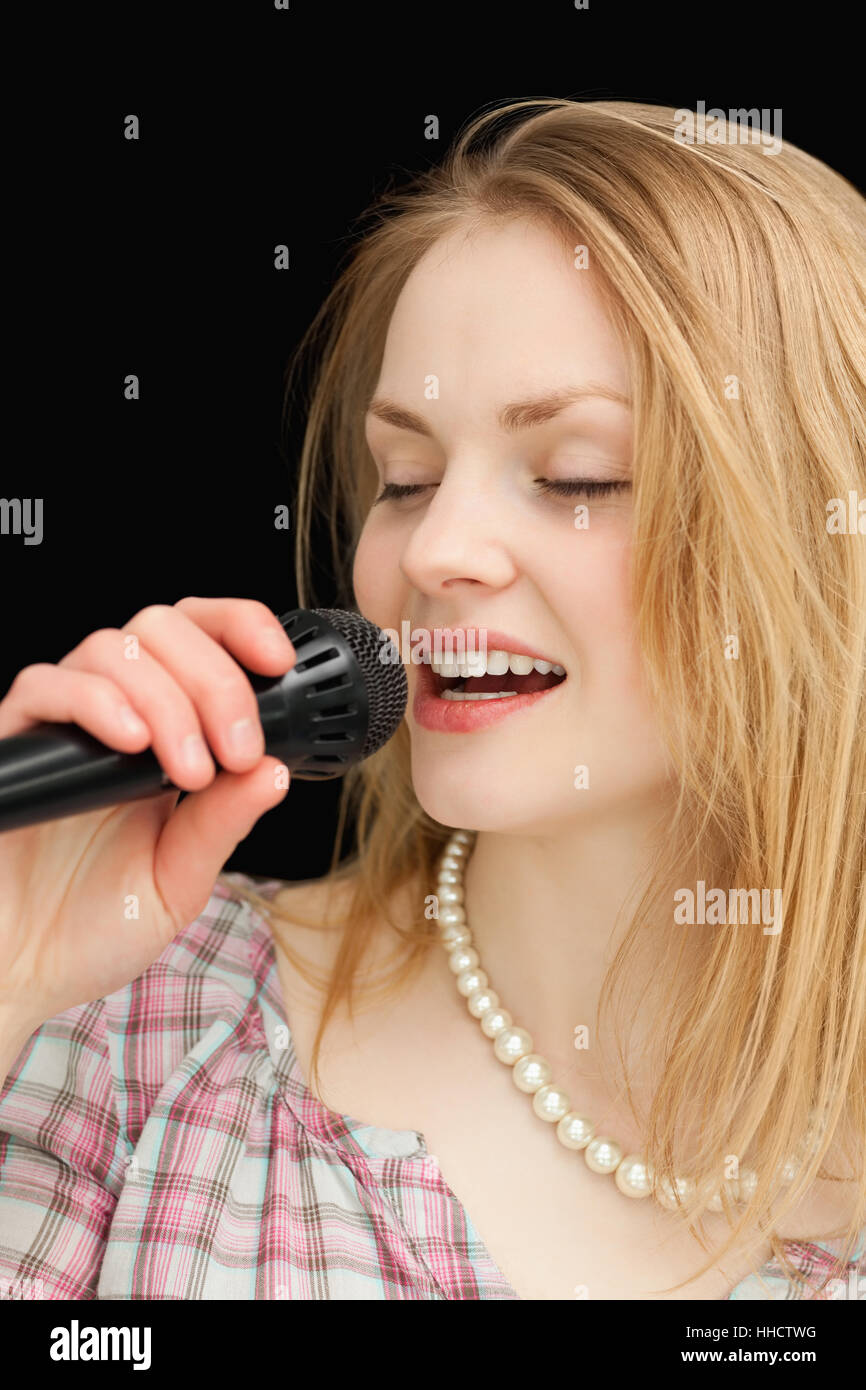 Woman singing while closing her eyes against black background Stock Photo