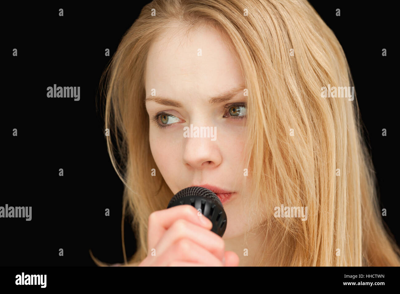 blond-haired woman singing against black background Stock Photo