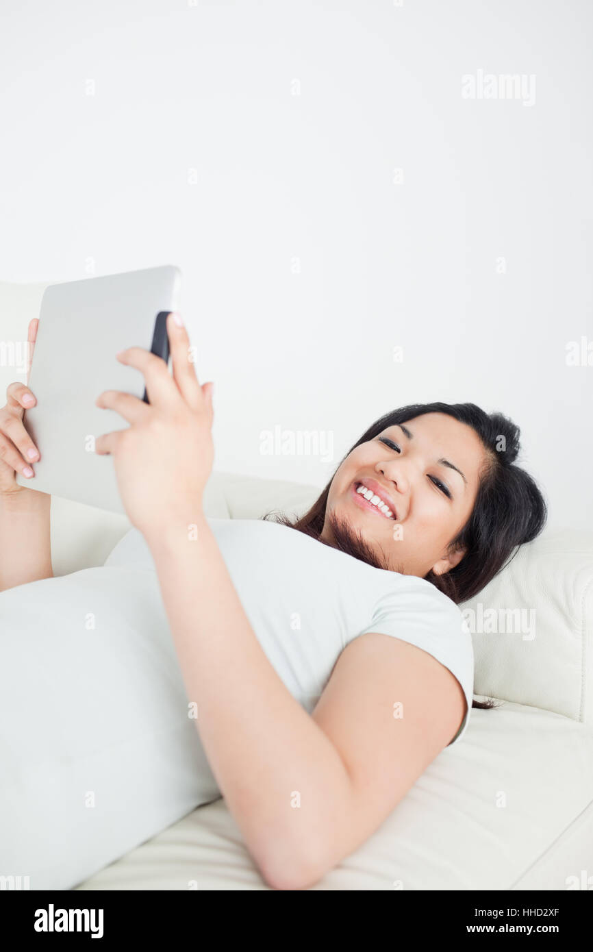Smiling woman lying on a sofa while holding a tactile tablet in a ...